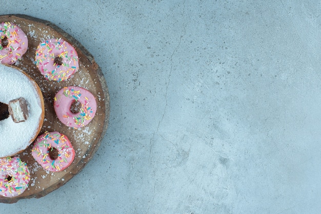 Donuts pequeños alrededor de un donut grande sobre una tabla de madera sobre mármol.