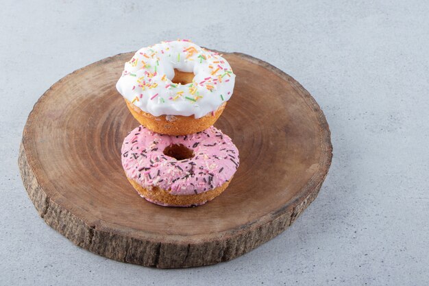 Donuts rosados y blancos decorados con chispitas sobre pieza de madera