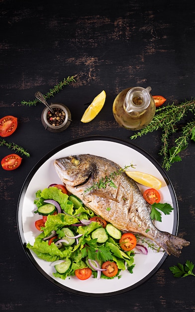 Dorado de pescado al horno con limón y ensalada fresca en plato blanco