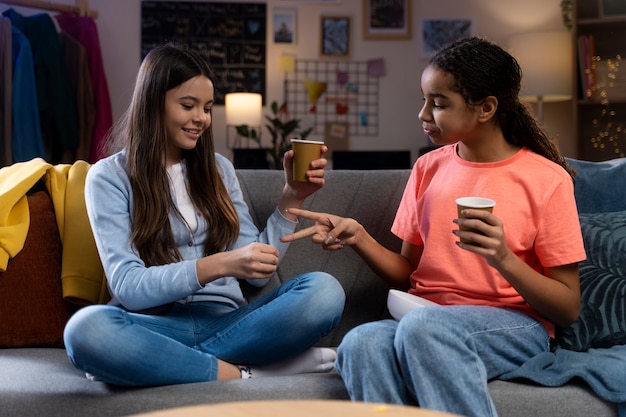 Dos adolescentes en casa bebiendo refrescos de tazas y divirtiéndose