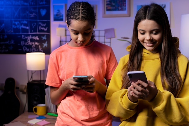 Dos adolescentes enviando mensajes de texto juntos en casa en teléfonos inteligentes