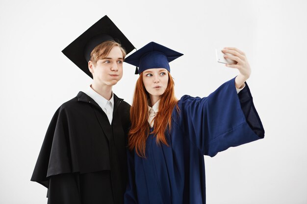 Dos alegres graduados de la universidad engañando haciendo selfie.
