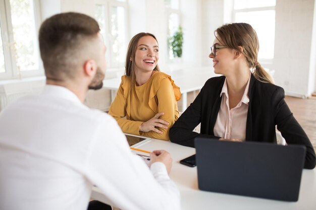 Dos alegres mujeres de negocios mirándose felizmente mientras pasan una entrevista de trabajo en una oficina moderna