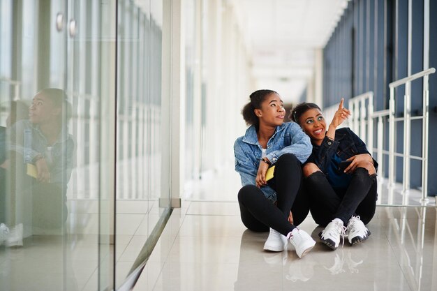 Dos amigas africanas con chaqueta de jeans sentadas juntas en el interior