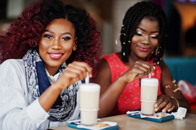 Dos amigas afroamericanas atractivas sentadas en la mesa en el café con café con leche