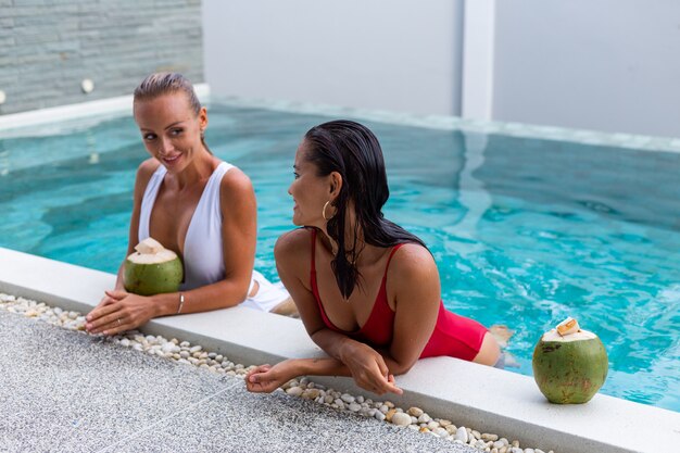 Dos amigas asiáticas y caucásicas con maquillaje en la piscina de la villa