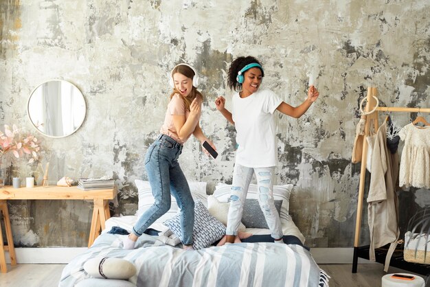 Dos amigas bailando juntas en la cama mientras escuchan música