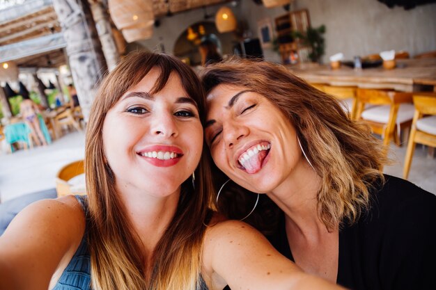 Dos amigas caucásicas europeas con maquillaje natural y pelo corto toman selfie en café de verano