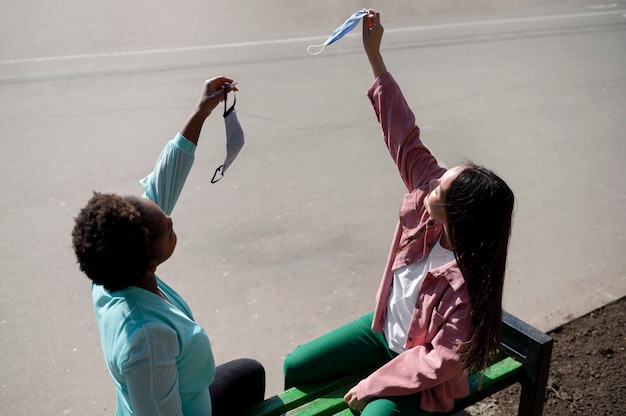 Dos amigas celebrando juntas el levantamiento de las restricciones de mascarillas al aire libre