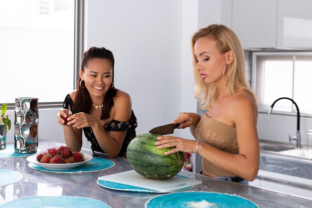 Dos amigas comiendo frutas tropicales de sandía y rambután en la cocina