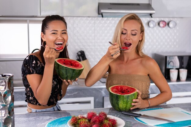 Dos amigas comiendo frutas tropicales de sandía y rambután en la cocina