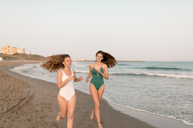 Foto gratuita dos amigas corriendo en la playa de arena