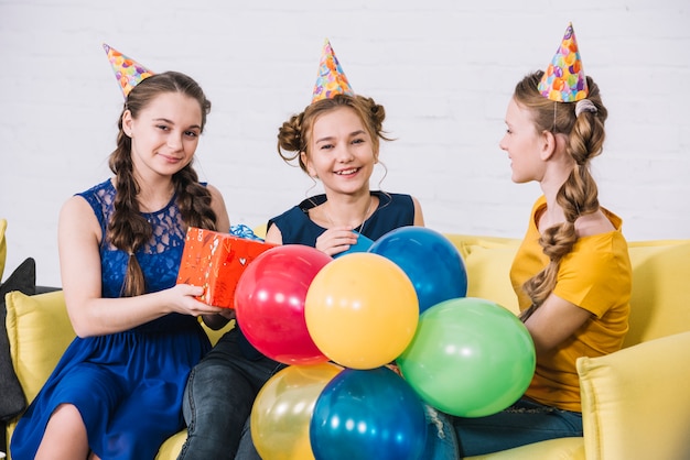 Dos amigas dando regalos a la cumpleañera sentada en un sofá amarillo