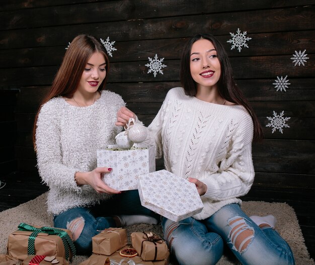 Dos amigas divertidas bastante jóvenes sonriendo y divirtiéndose, sosteniendo regalos navideños, listos para la celebración.