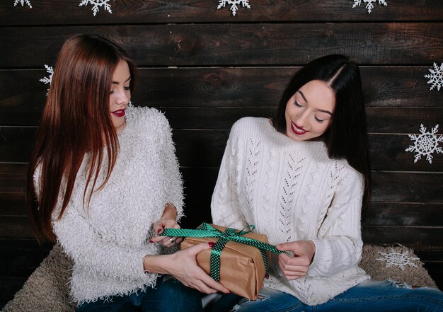 Dos amigas divertidas bastante jóvenes sonriendo y divirtiéndose, sosteniendo regalos navideños