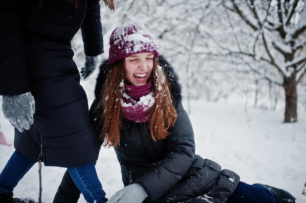 Dos amigas divertidas divirtiéndose en el día nevado de invierno cerca de árboles cubiertos de nieve