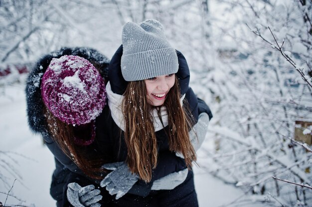 Dos amigas divertidas divirtiéndose en el día nevado de invierno cerca de árboles cubiertos de nieve