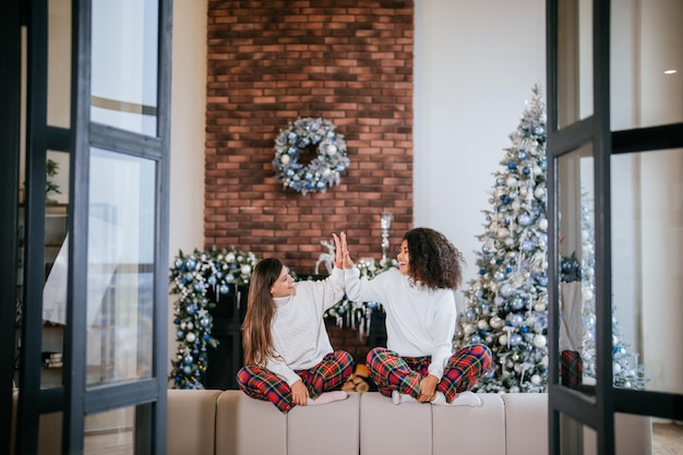 Foto gratuita dos amigas estudiantes sentados en el sofá en casa choca esos cinco