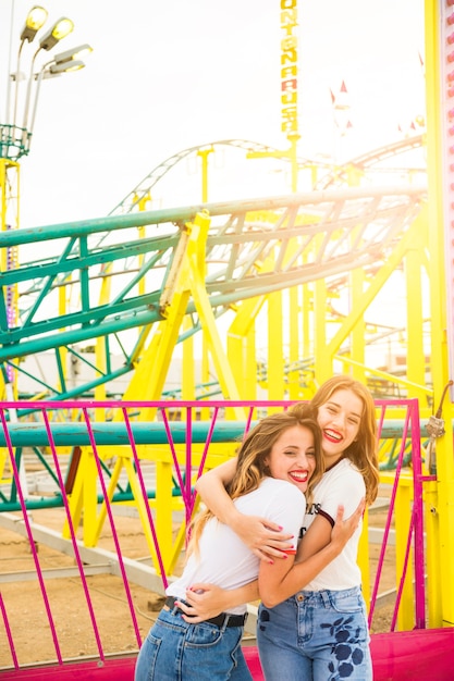 Dos amigas felices que se abrazan frente a la montaña rusa