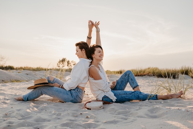 Dos amigas jóvenes divirtiéndose en la playa al atardecer, romance de amor lesbiana gay