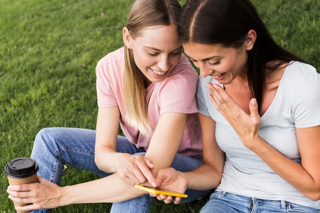 Dos amigas mirando a través del teléfono inteligente al aire libre