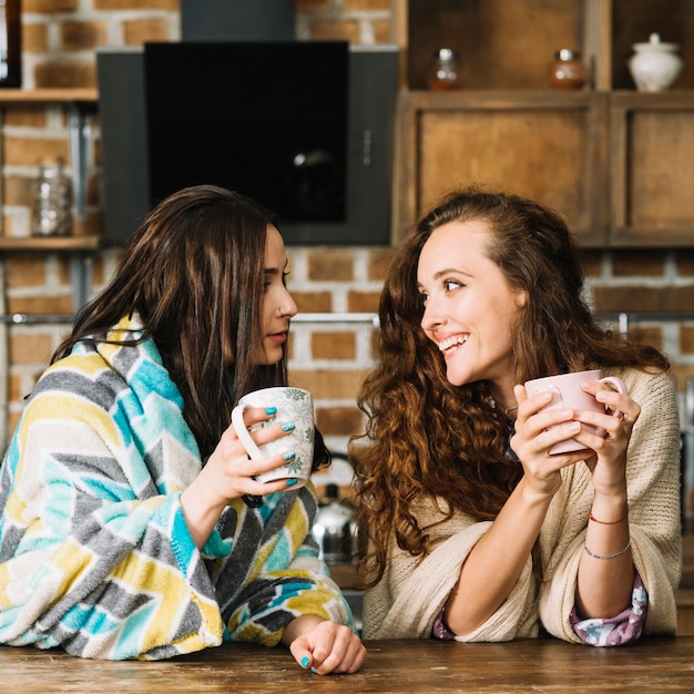 Dos amigas mirándose mientras beben una taza de café