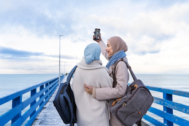 Dos amigas musulmanas con hijabs tomándose una selfie mientras viajan