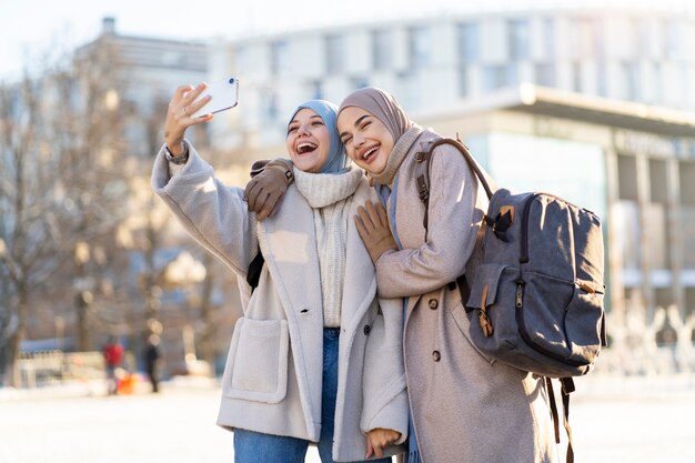 Dos amigas musulmanas tomándose una selfie mientras viajan por la ciudad