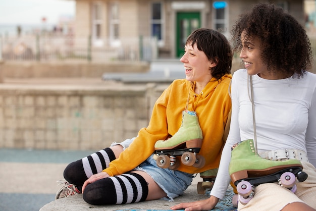 Foto gratuita dos amigas con patines hablando y riendo al aire libre