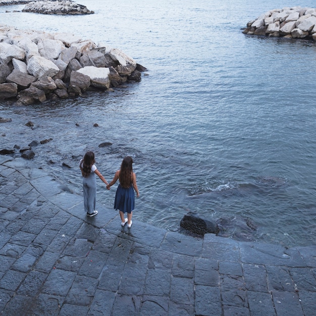 Foto gratuita dos amigas de pie cerca de la costa cogidos de la mano