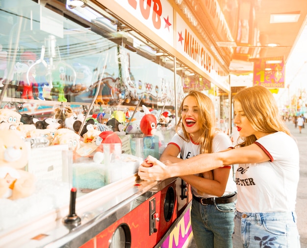 Dos amigas de pie cerca de la tienda de juguetes en el parque de atracciones