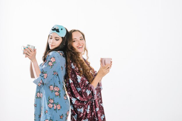 Dos amigas de pie espalda con espalda sosteniendo una taza de café