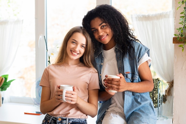 Dos amigas posando junto con tazas en la cocina