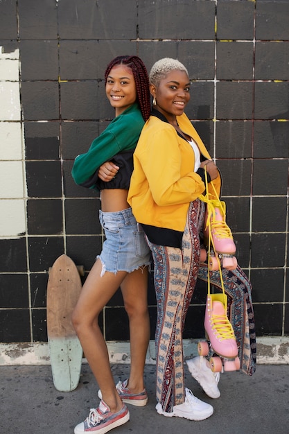 Foto gratuita dos amigas posando con su monopatín y patines en la ciudad