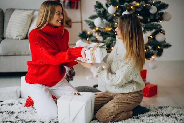 Dos amigas con regalos de navidad por el árbol de navidad