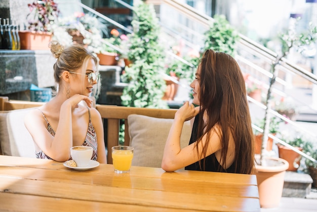 Dos amigas sentadas juntas en caf��� mirándose
