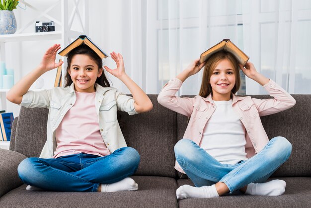 Dos amigas sentadas en un sofá gris con un libro sobre su cabeza