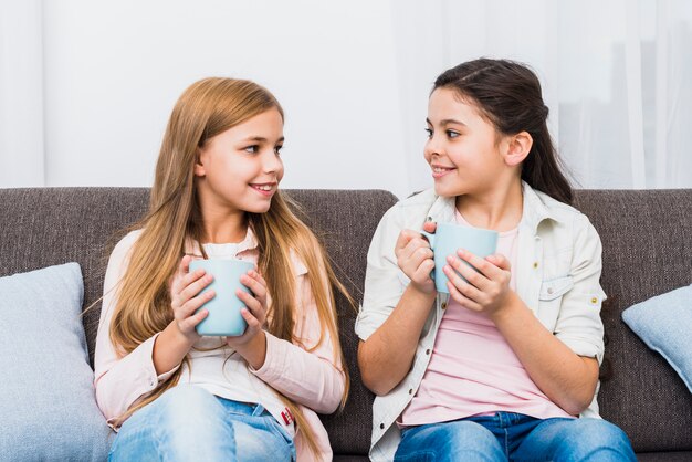 Dos amigas sentadas en el sofá sosteniendo la taza de café en la mano mirando el uno al otro