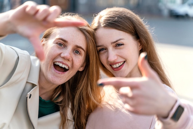 Dos amigas sonrientes al aire libre en la ciudad fingiendo tomar un selfie