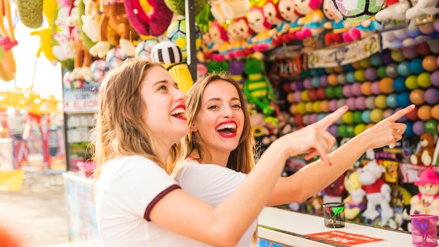 Dos amigas sonrientes que señalan el dedo en el parque de atracciones