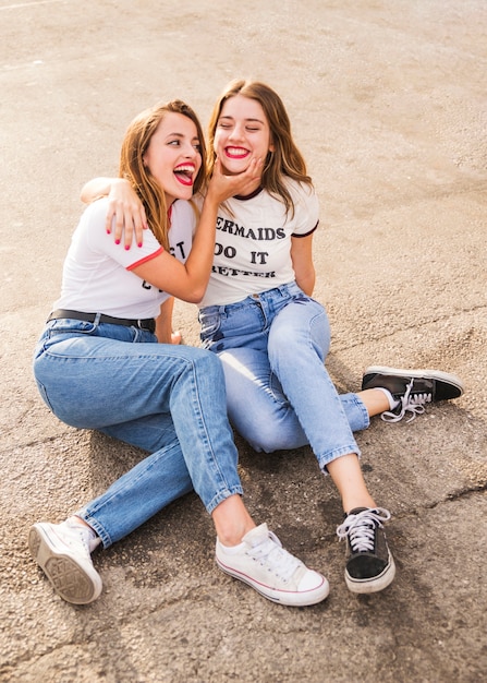 Dos amigas sonrientes sentados en el pavimento