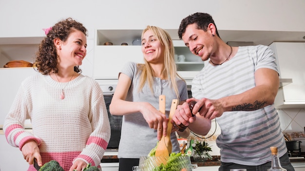 Dos amigas y su hombre preparando ensalada en la cocina