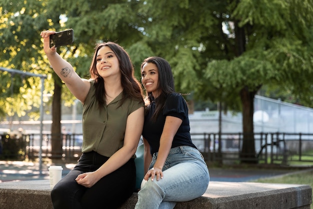 Dos amigas tomando selfie en el parque mientras toma un café