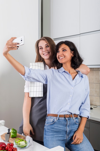 Dos amigas tomando selfie en el teléfono móvil en la cocina