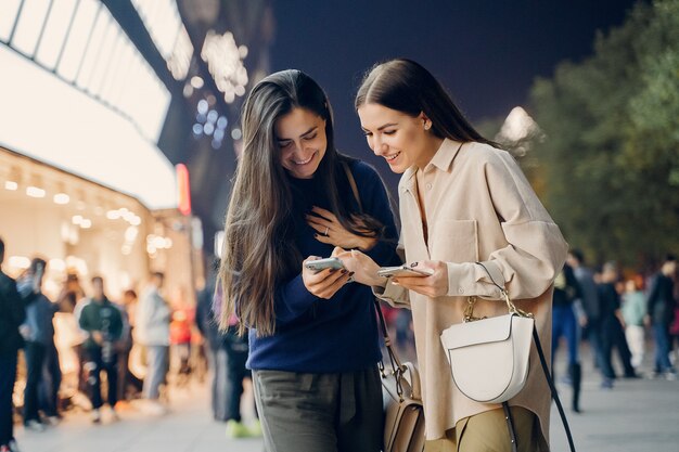 Dos amigas usando su teléfono celular mientras exploran una nueva ciudad por la noche