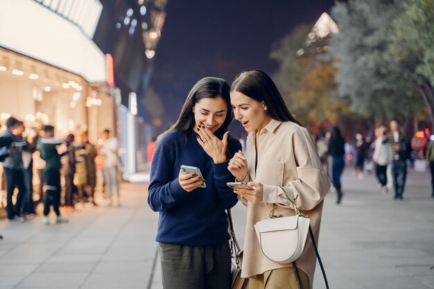 Dos amigas usando su teléfono celular mientras exploran una nueva ciudad por la noche