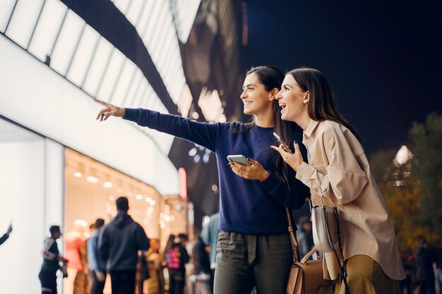 Dos amigas usando su teléfono celular mientras exploran una nueva ciudad por la noche