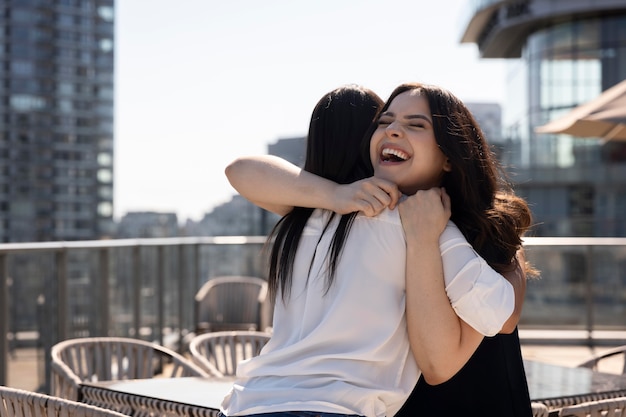 Foto gratuita dos amigas viéndose en una terraza en la azotea y abrazándose