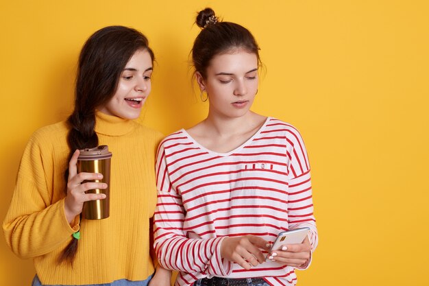 Dos amigos compartiendo teléfonos inteligentes y tomando café juntos, posando