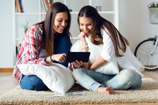 Dos amigos hermosos de la mujer joven que usan la tableta digital en el país.